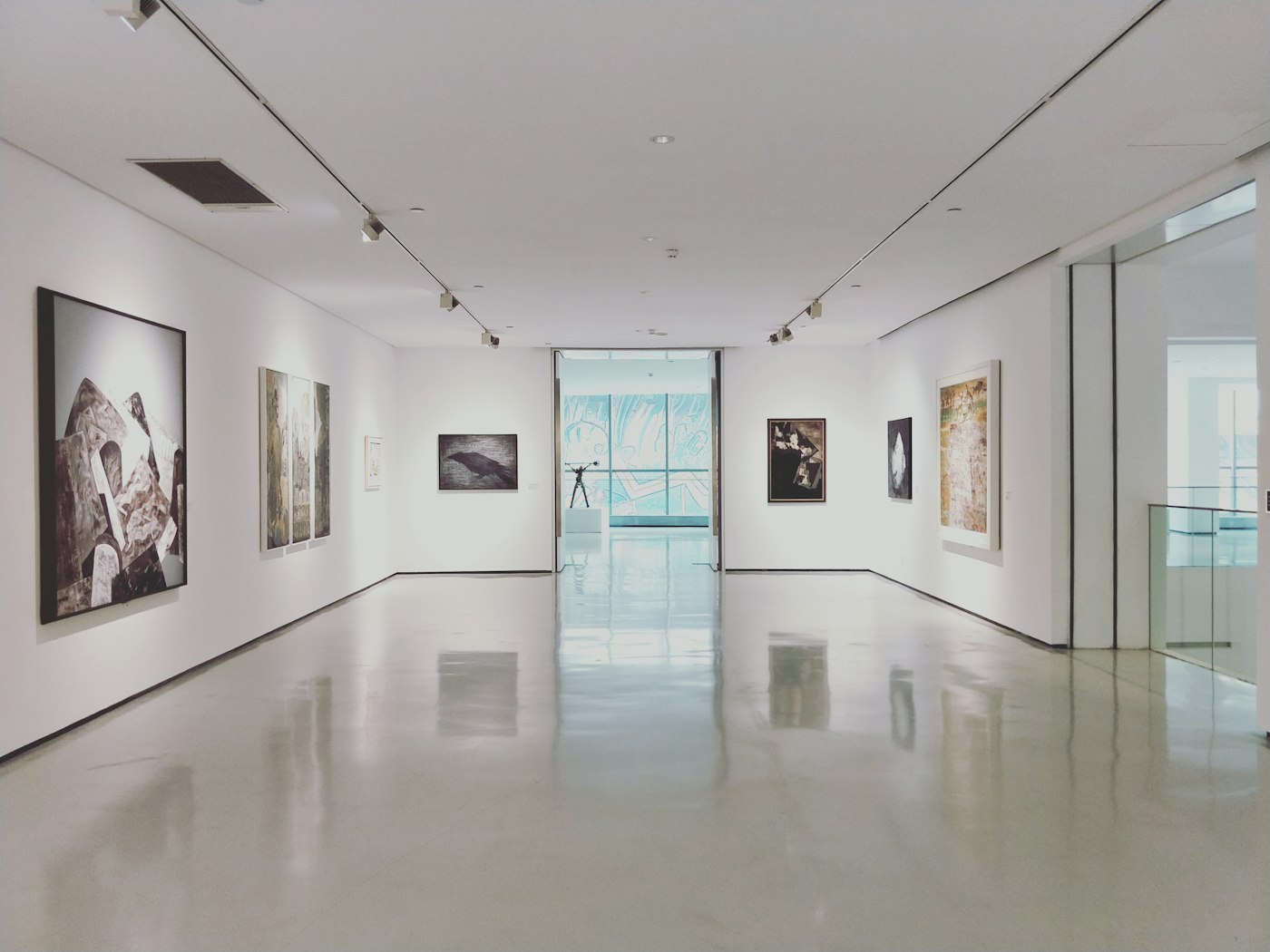 A bright gallery interior with paintings hung on white walls.